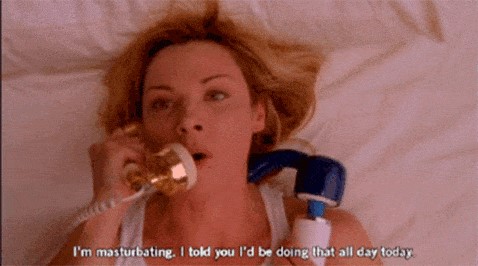 Woman is lying down with a vibrator in her hand, speaking into the phone, “I’m masturbating. I told you I’d be doing that all day today.”
