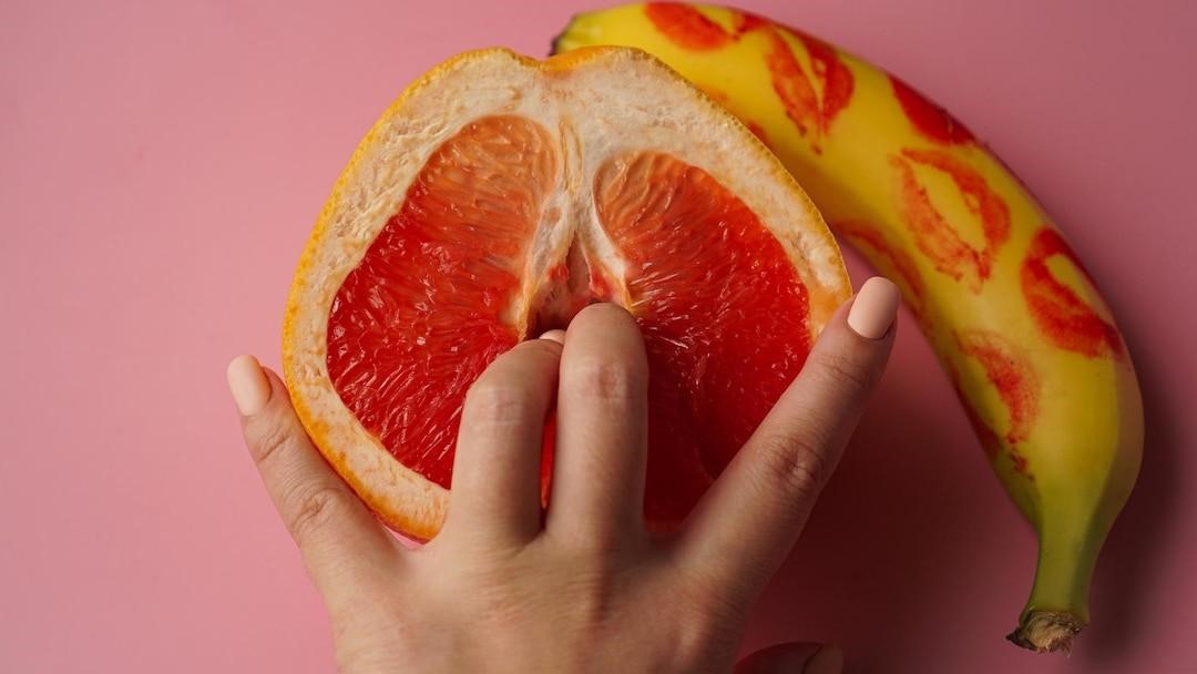 Fingers inserted inside an orange and a banana with lipstick stains at the side.